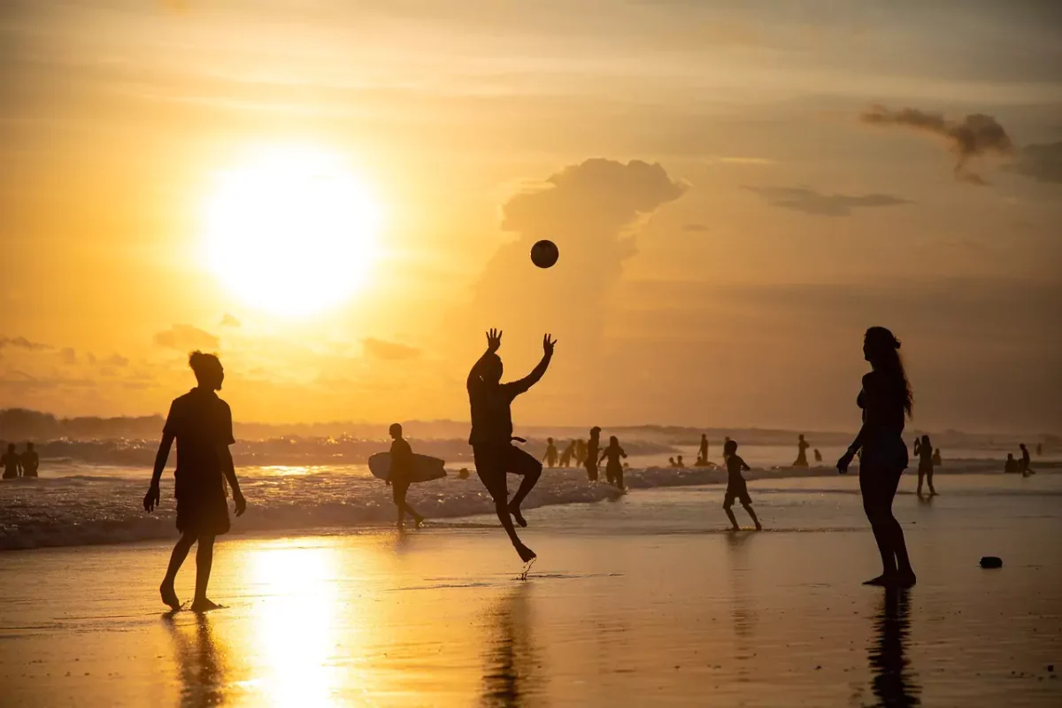 A group of people playing volleyball on the beach at sunset.