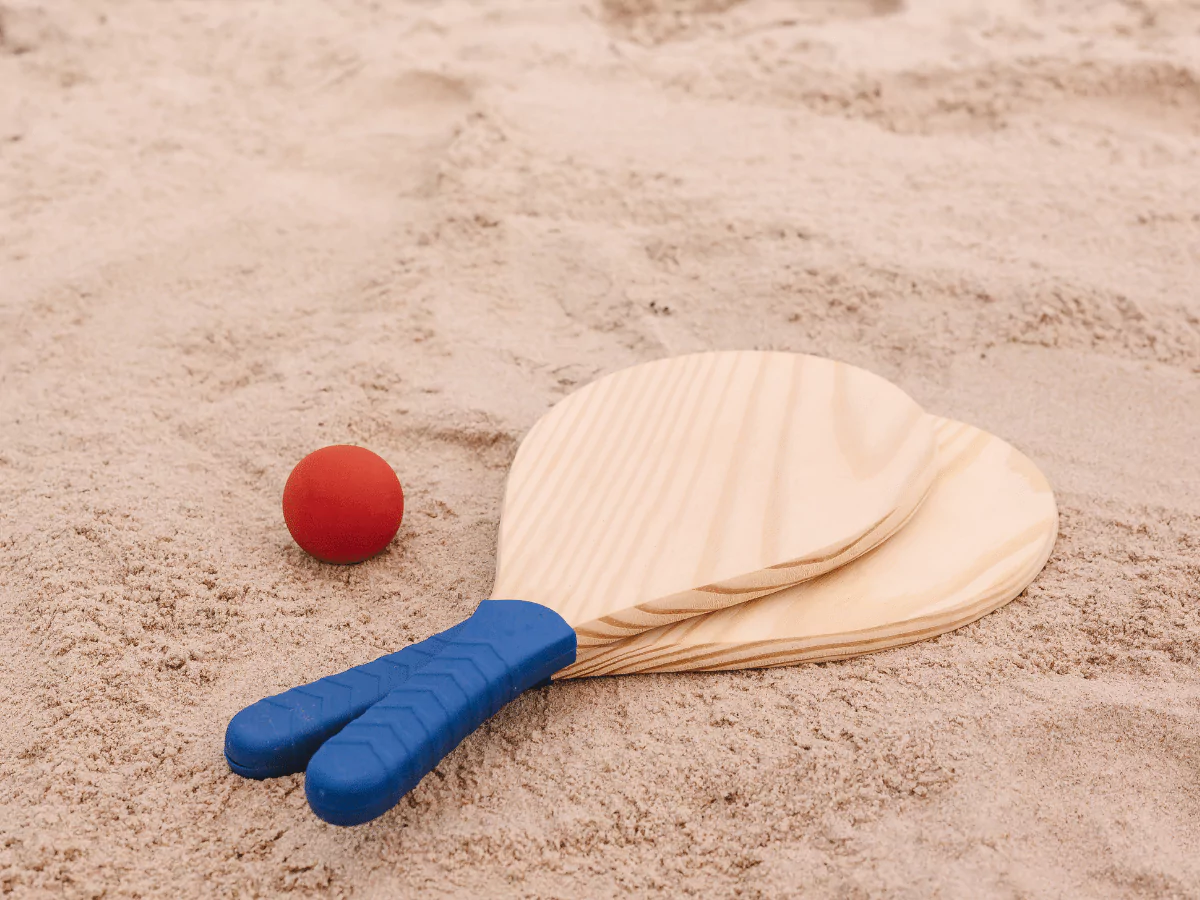 2 beach paddles and red paddle game ball in the sand