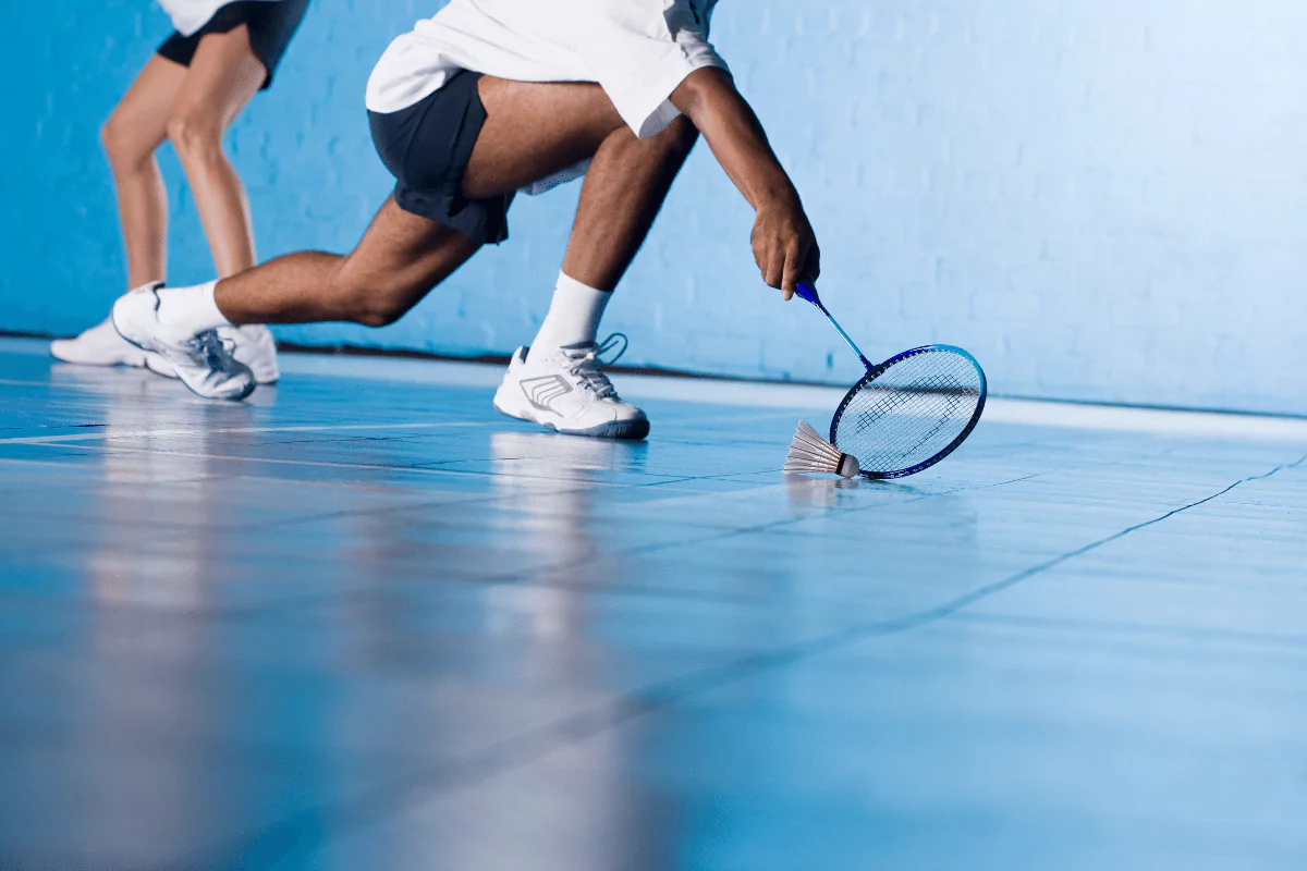 badminton racquet hitting shuttlecock off ground, blue floor