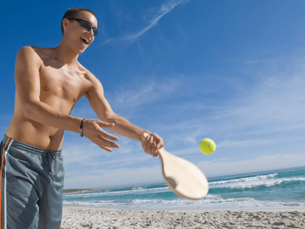 man hitting ball on the beach with a paddle