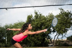 woman hitting shuttlecock over net with racket