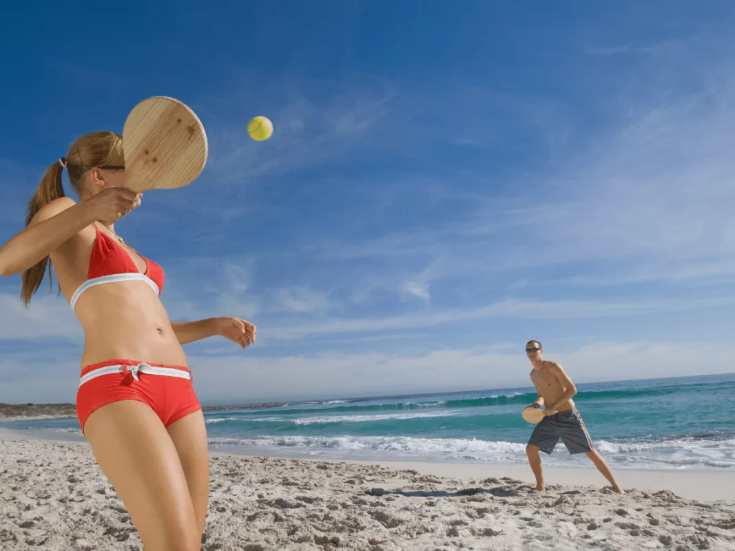 A man and a woman playing beach paddle ball on the beach.