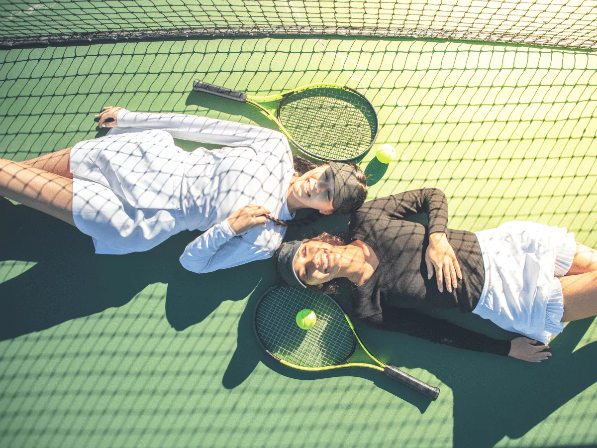 2 women laying on tennis court, 2 tennis rackets
