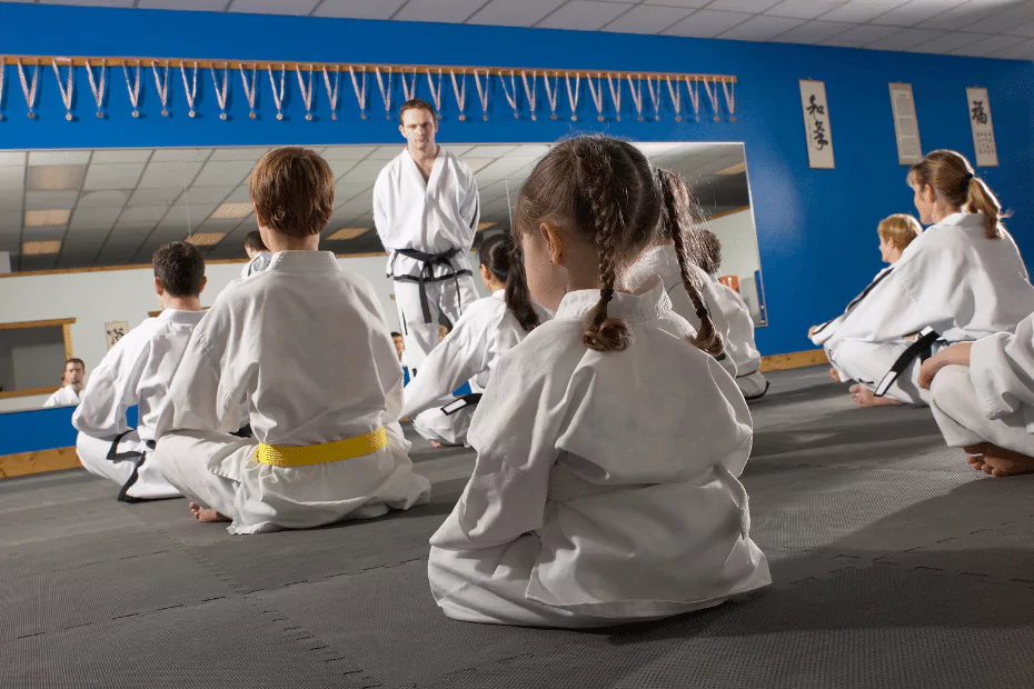 karate class. children in white martial arts robes sitting in front of instructor. gray mat