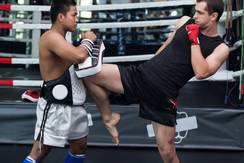 A man wearing muay thai gear kicks a kick in a boxing ring