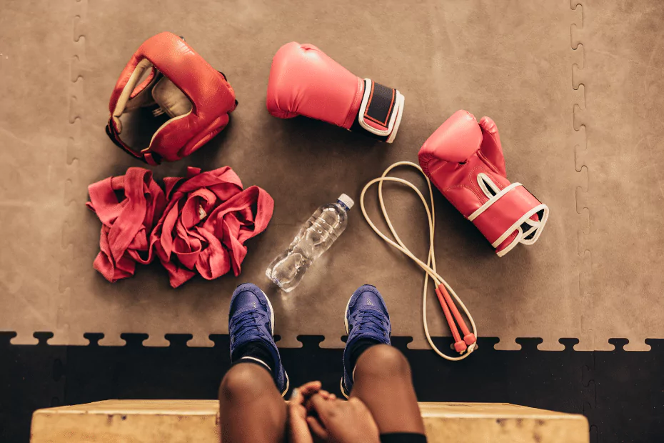 A woman's feet on a boxing mat with boxing gloves and a bottle of water, demonstrating the sport of boxing