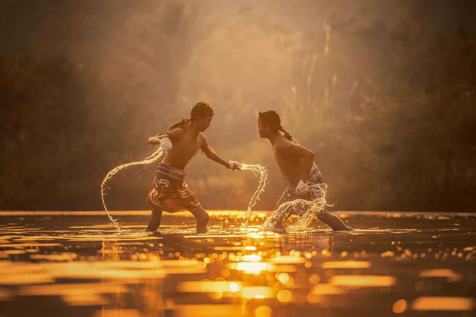 Two boys wearing muay thai gear playing in the water at sunset