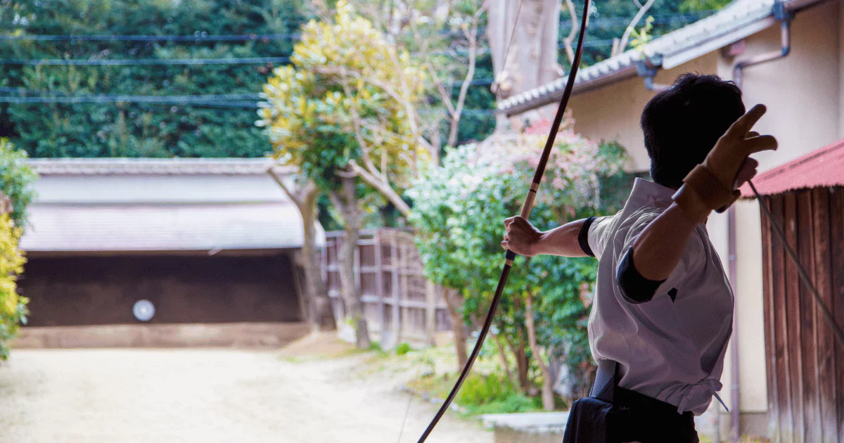 A man mastering Kyudo, a Japanese archery art, in front of a house