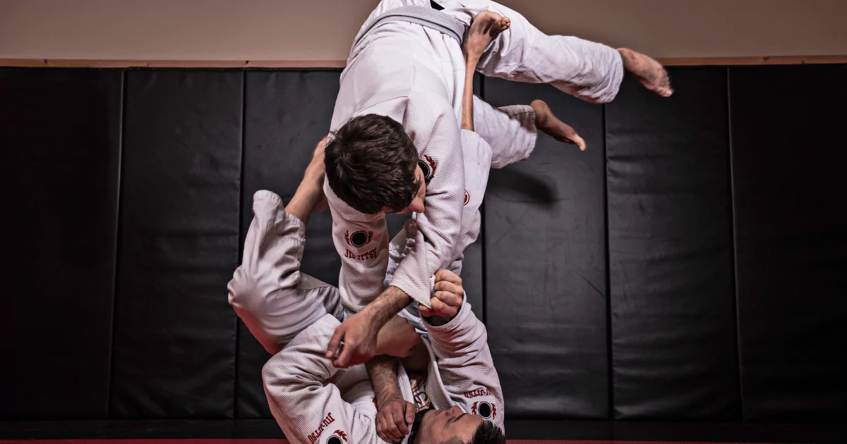 Keywords: Brazilian Jiu Jitsu, BasicsModified Description: Two men practicing basic Brazilian Jiu Jitsu moves in a gym
